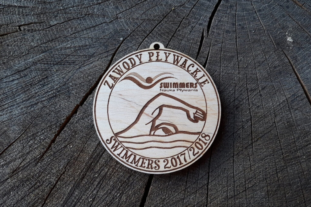 Drewniane medale na Zawody Pływackie Swimmers 2017/2018 z nagrawerowanym motywem fal, pływaka i grawerem logotypu.