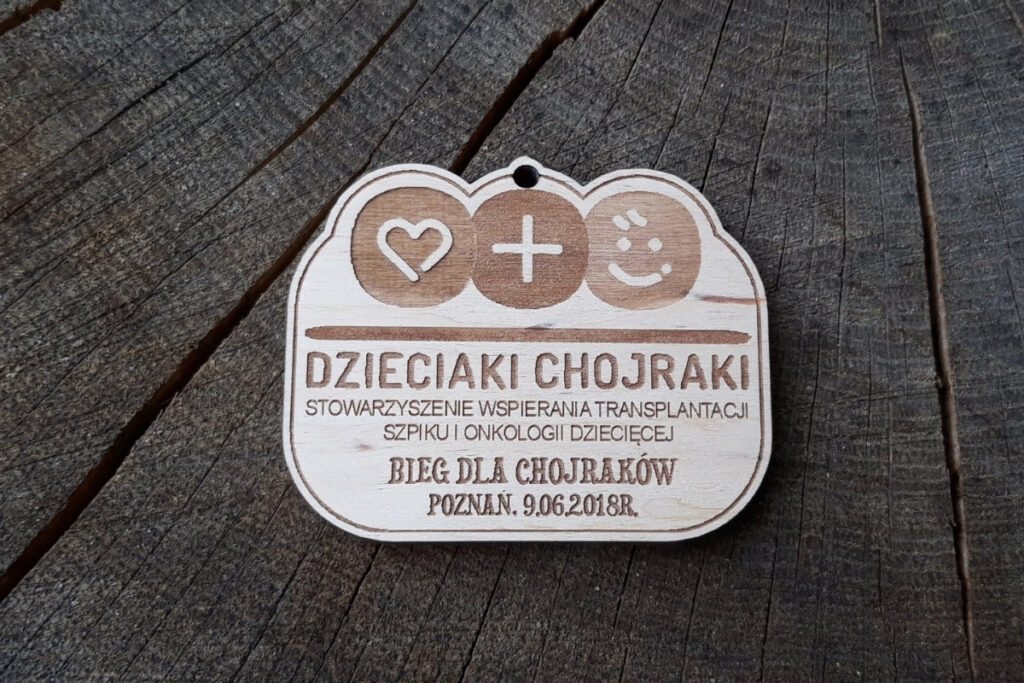 Medal wykonany z jasnego drewna z grawerowanym logiem fundacji Dzieciaki Chojraki.