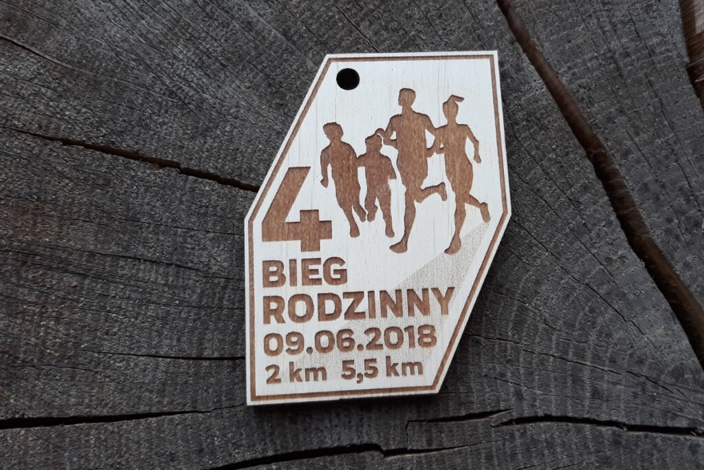 Pamiątkowy medal z drewna o naturalnym wykończeniu, przedstawiający biegnących sportowców i napis 4 Bieg Rodzinny, oraz datę.