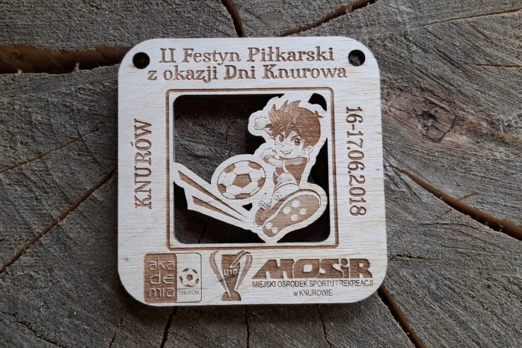 Drewniany ażurowy medal piłkarski na II Festyn Piłkarski w Knurowie z wyciętym humorystycznym motywem piłki i młodego piłkarza