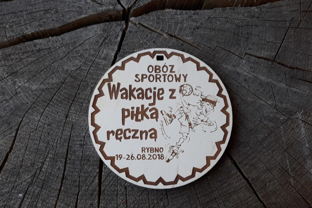 Drewniany medal sportowy z motywem piłki ręcznej przygotowany na wakacyjny obóz w Rybnie.