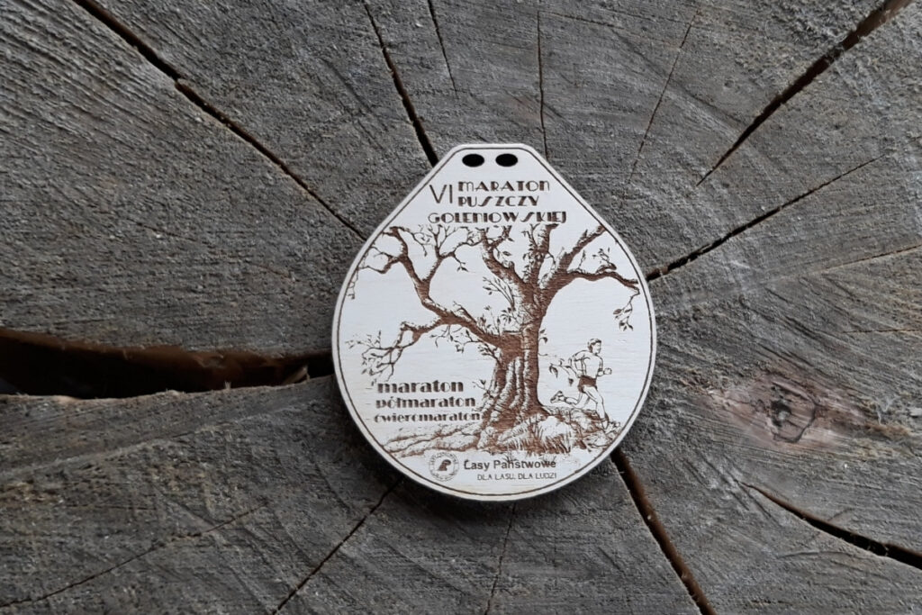 Drewniany medal sportowy na VI Maraton Puszczy Gołębiowskiej z grawerem logotypu biegu i motywem drzewa.