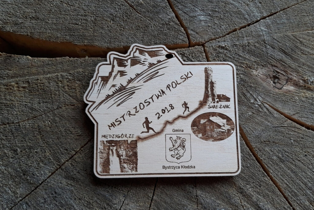 Drewniany medal na Mistrzostwa Polski Międzygórze Śnieżnik 2018 z grawerem logotypu zawodów i górskim motywem.