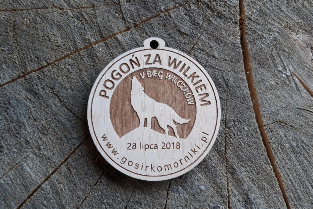 Drewniany medal dla dzieci na V Bieg Wilczków z grawerem wilka i napisem „Pogoń za Wilkiem”.