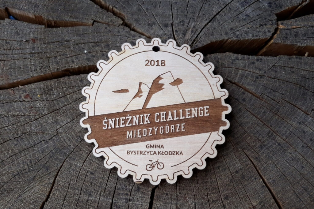 Drewniany medal pamiątkowy Śnieżnik Challenge Międzygórze z grawerem logotypu zawodów i motywem górskim.