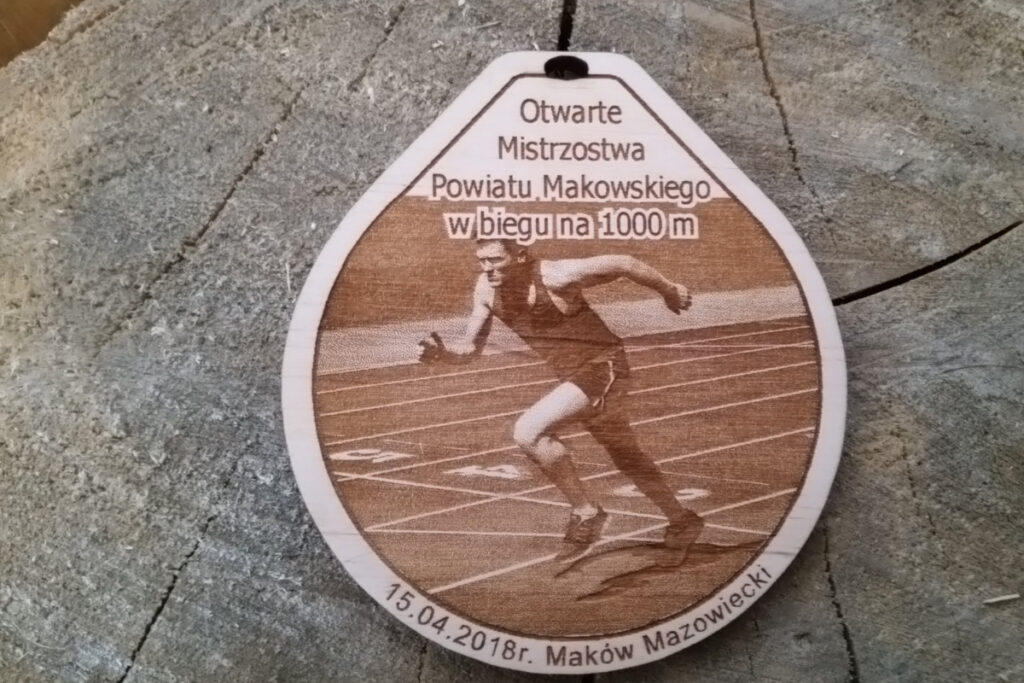 Drewniany medal na Otwarte Mistrzostwa Powiatu Makowskiego w biegu na 1000m, z grawerem biegnącego zawodnika.
