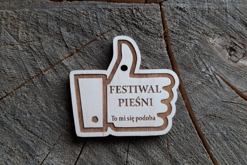 Drewniany medal w kształcie kciuka z napisem „To mi się podoba” przygotowany na Festiwal Pieśni.
