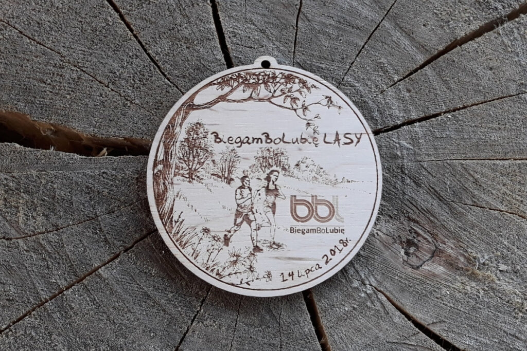 Drewniany medal sportowy z logotypem BiegamBoLubię Lasy i motywem drzew, wykonany techniką grawerowania laserowego.