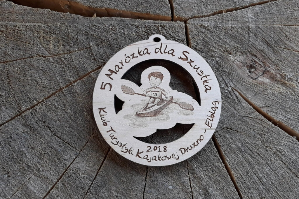 Drewniany medal ażurowy z sylwetką kajakarza na falach, propozycja na 5. spływ kajakowy rzeką Marózką.