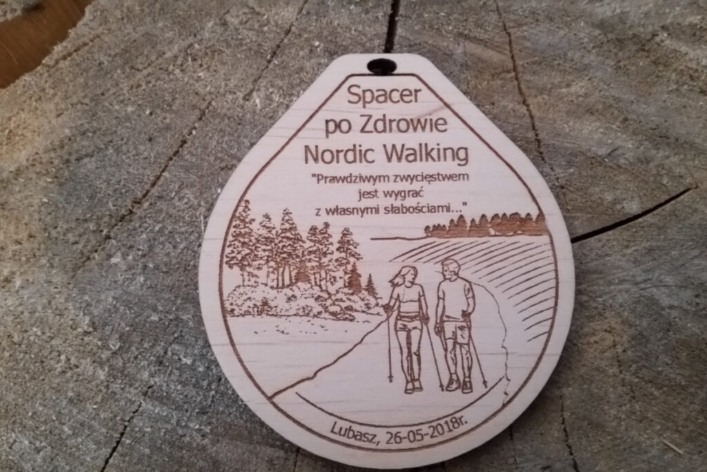 Drewniany medal z grawerem przedstawiającym postać uprawiającą Nordic Walking, napisem „Spacer po Zdrowie”.