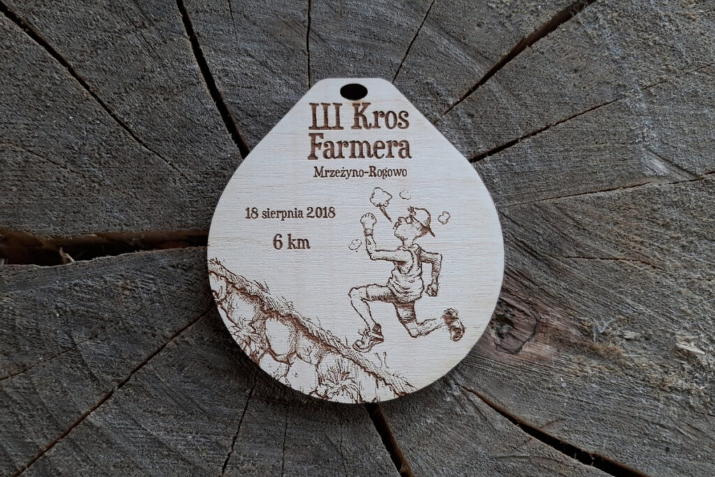 Humorystyczny drewniany medal na III Kros Farmera z zabawnym grawerem biegacza biegnącego pod górkę.