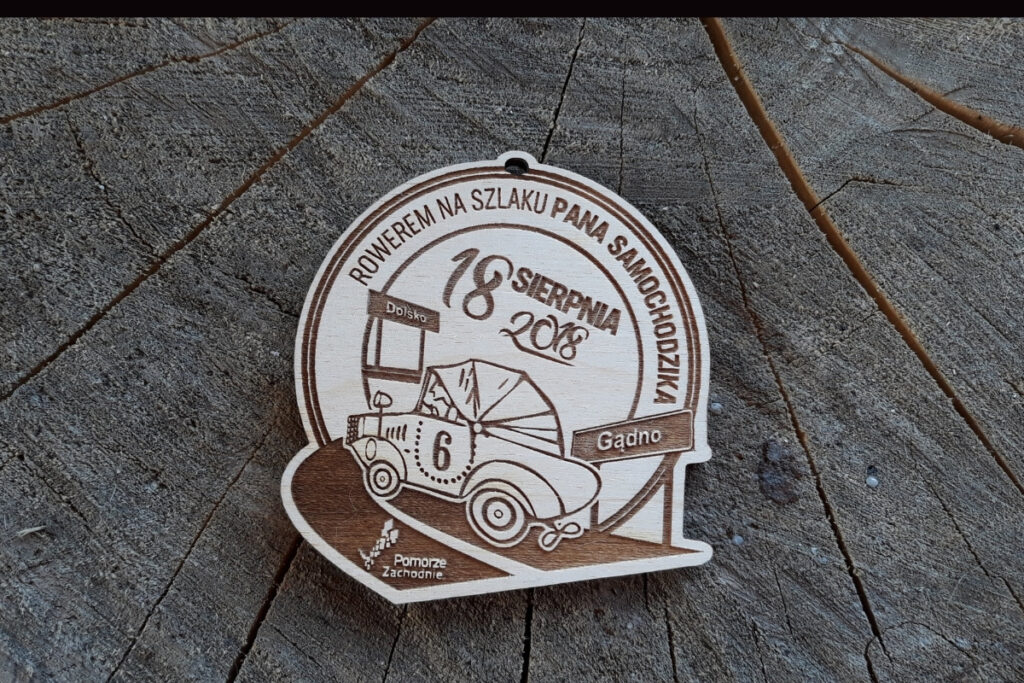 Drewniany medal rajdowy z grawerem roweru i napisem „Rowerem na szlaku Pana Samochodzika”.