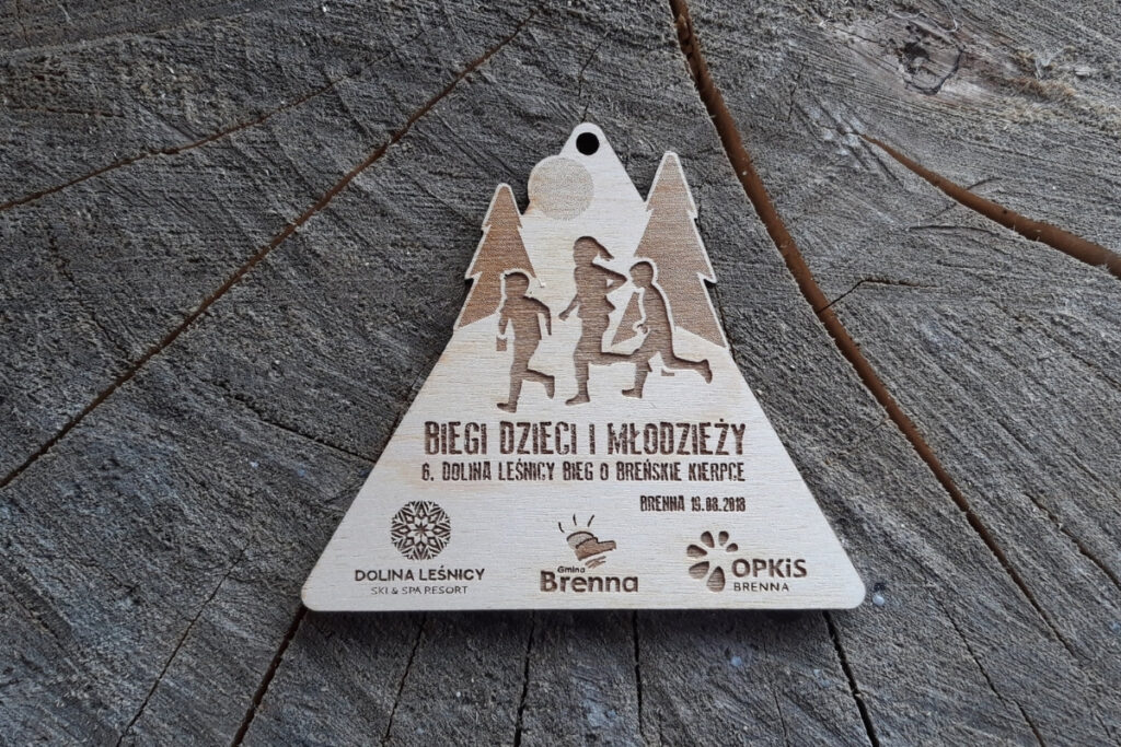 Drewniany medal dla dzieci z radosnym grawerem biegnących postaci i napisem „Biegi Dzieci i Młodzieży.