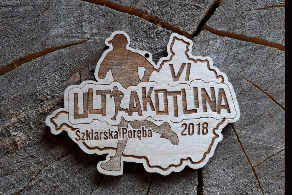 Drewniany medal na Ultrakotlinę z grawerem sylwetki biegacza i zarysem trasy biegu.