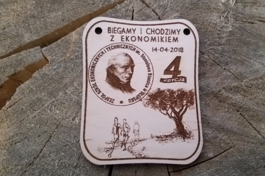 Prostokątny drewniany medal z grawerem „Biegamy i chodzimy z Ekonomikiem”, ozdobiony motywami sportowymi i logo szkoły, zawieszony na ekologicznym sznurku.