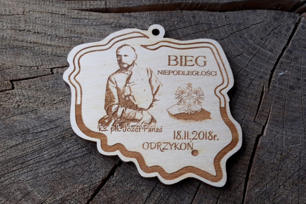 Drewniany medal w kształcie konturu Polski z grawerowaną podobizną ks. płk. Józefa Panasia na Bieg Niepodległości.