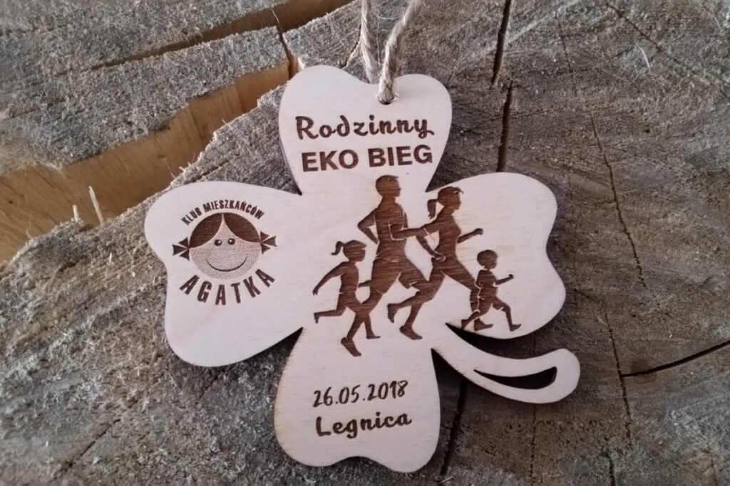 Drewniany medal z napisem Rodzinny Eko Bieg, w kształcie czterolistnej koniczyny.