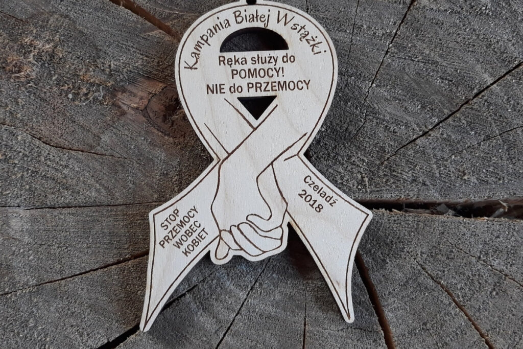 Drewniany medal w kształcie wstążki z grawerem splecionych dłoni na Kampanię Białej Wstążki.