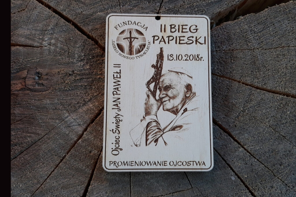 Drewniany medal na II Bieg Papieski z grawerem logotypu Fundacji Dzieło Nowego Tysiąclecia i grawerem podobizny Papieża Jana Pawła II
