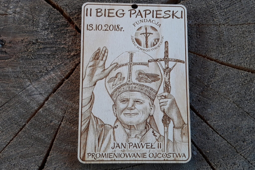 Drewniany medal na II Bieg Papieski z grawerem logotypu Fundacji Dzieło Nowego Tysiąclecia i grawerem podobizny Papieża Polaka Jana Pawła II
