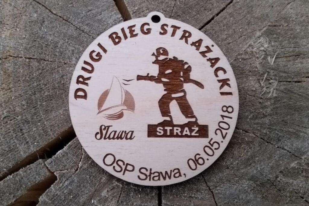 Okrągły drewniany medal z grawerem biegnącego strażaka i napisem "II Bieg Strażacki OSP Sława 20.05.2018".