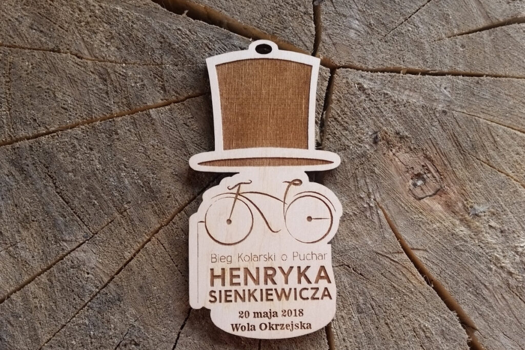 Drewniany medal na Bieg Kolarski o Puchar Henryka Sienkiewicza z grawerowanym kapeluszem i rowerem.
