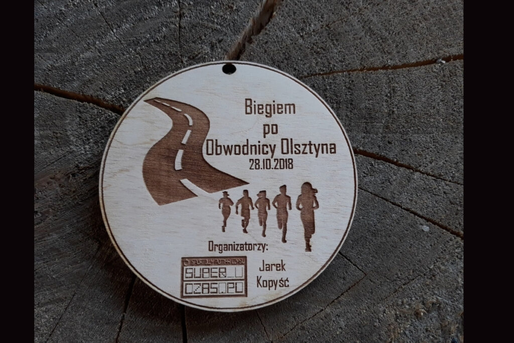 Drewniany medal na wydarzenie „Biegiem po obwodnicy Olsztyna” z grawerem drogi i logotypu.