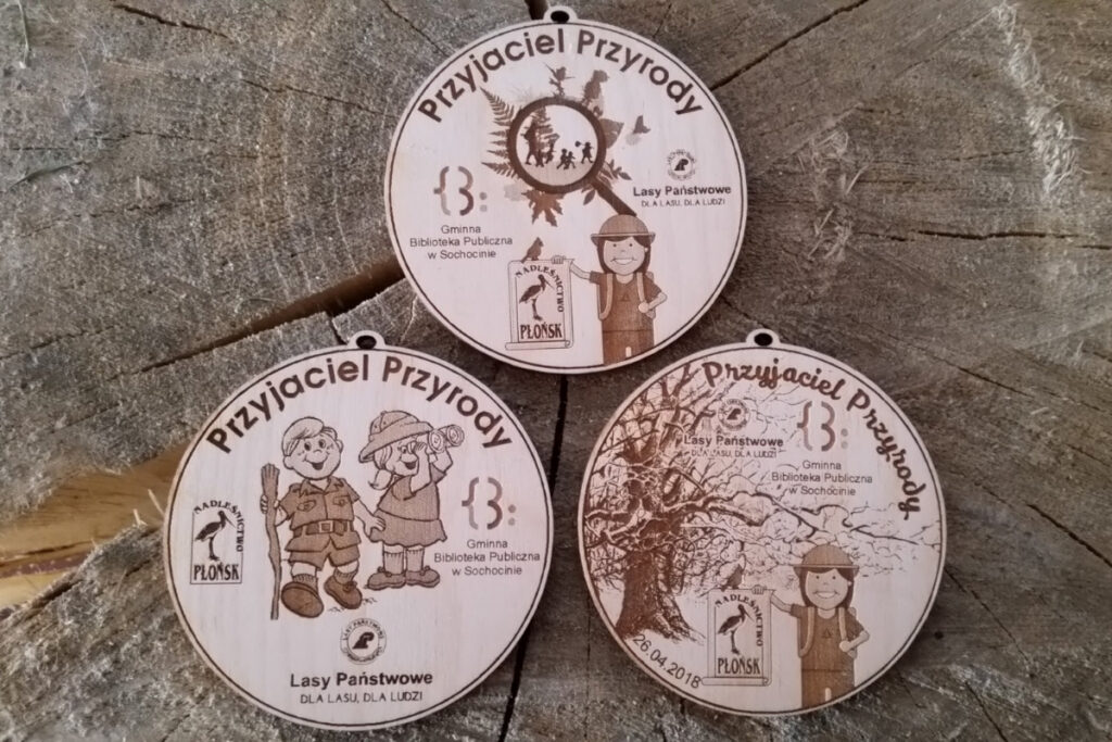 Ekologiczny medal dla dzieci wykonany z jasnego drewna. Na tarczy grawerowany uśmiechnięty Przyjaciel Przyrody.