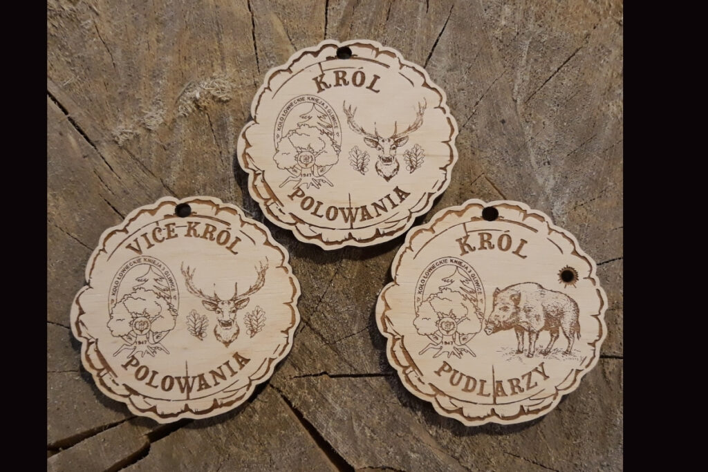 Zestaw drewnianych medali myśliwskich: Król Polowania, Vice-Król oraz Król Pudlarzy z grawerem wieńca jelenia lub dzika i logotypem.