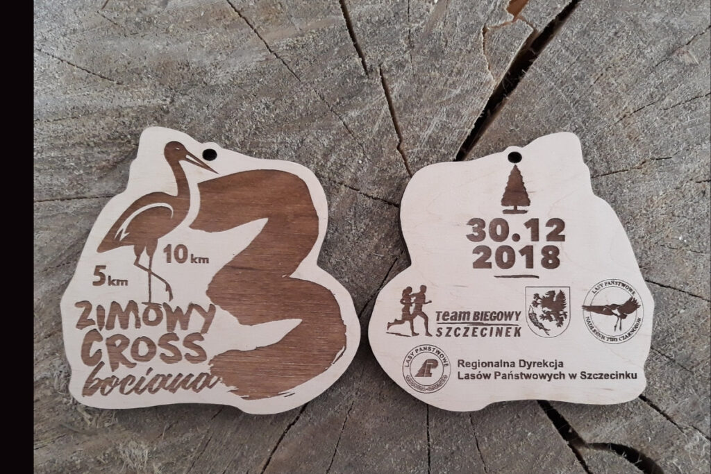 Dwustronny drewniany medal na 3. Zimowy Cross Bociana z grawerem logotypu biegu i partnerów.