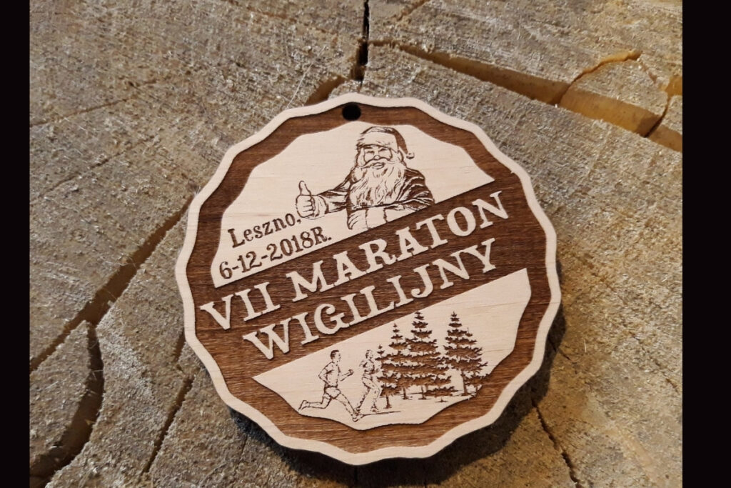 Drewniany medal na VII Maraton Wigilijny w Lesznie z grawerem sosen, biegaczy i mikołaja.