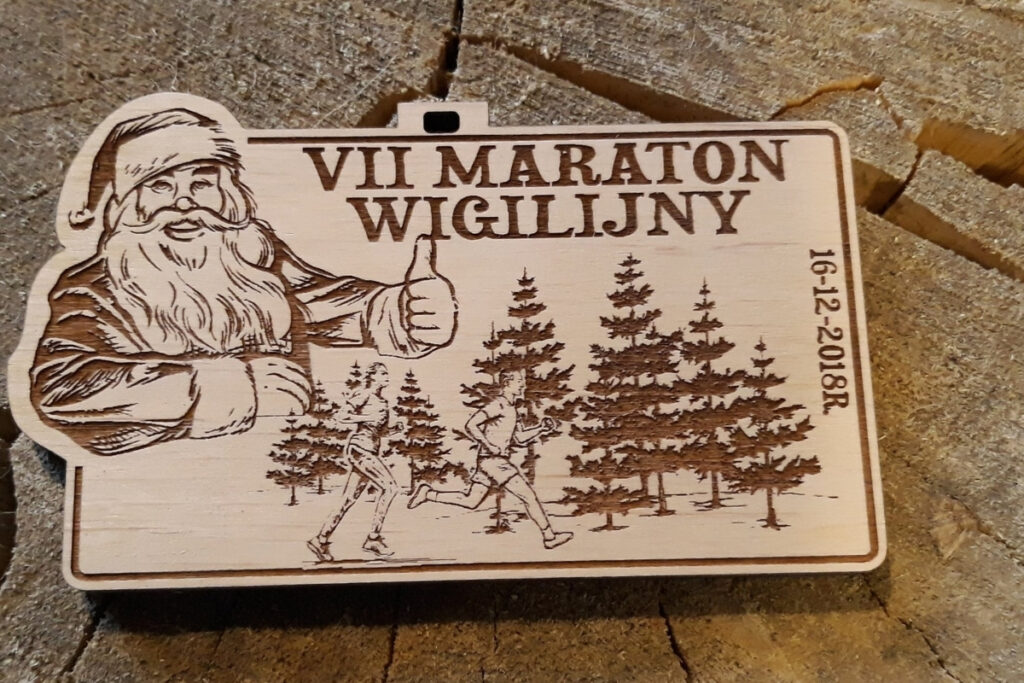 Drewniany medal na VII Maraton Wigilijny w Lesznie z grawerem sosen, biegaczy i mikołaja.