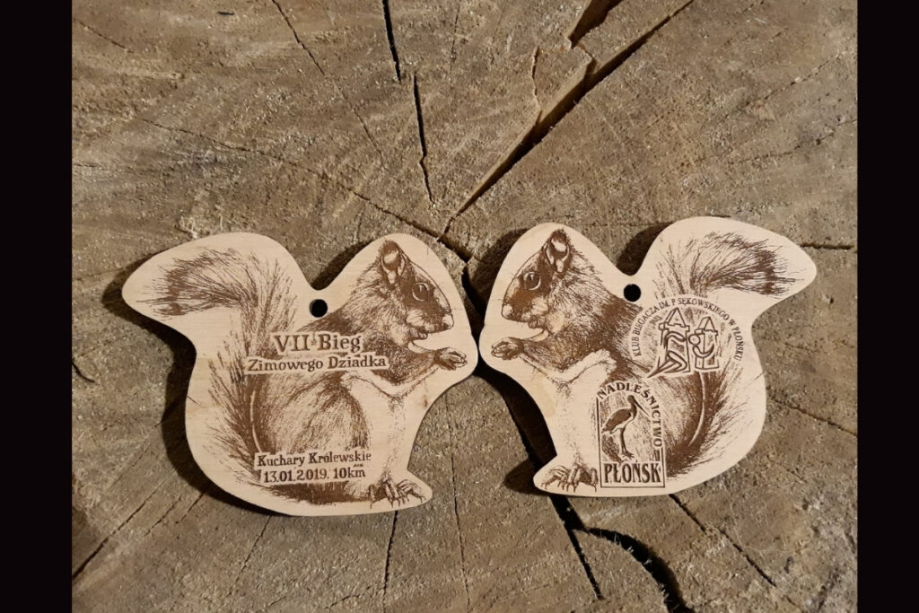 Dwustronny drewniany medal na VII Bieg Zimowego Dziadka z grawerem wiewiórki i logotypami.