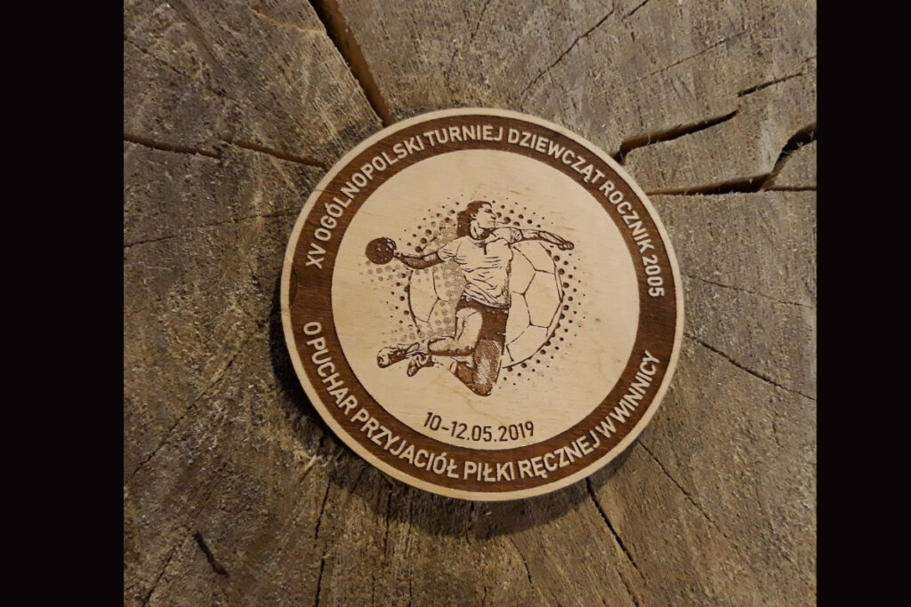 Drewniany medal na XV Ogólnopolski Turniej Piłki Ręcznej z grawerem zawodnika rzucającego piłkę.