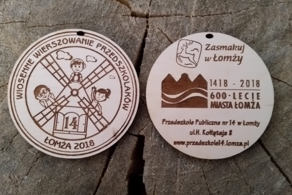 Okrągły drewniany medal dwustronny z napisem na rewersie "wiosenne wierszowanie przedszkolaków" a na rewersie z logotypami "zasmakuj w Łomży" i logiem 600-lecia Miasta Łomży.