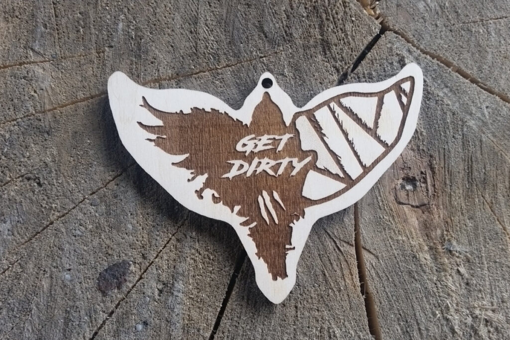 Drewniany medal w kształcie lecącego ptaka z napisem Get Dirty.