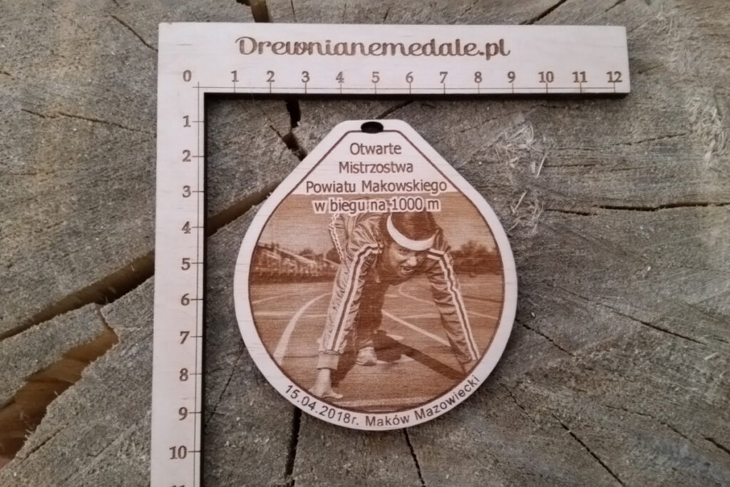 Drewniany medal sportowy z grawerem biegacza na bieżni lekkoatletycznej, zawieszony na ekologicznym sznurku.