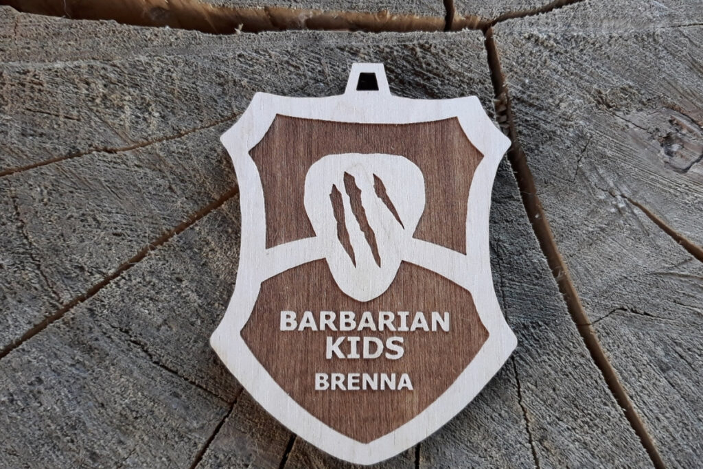 Drewniany medal Barbarian Kids Brenna w kształcie tarczy z dziurką na sznurek.