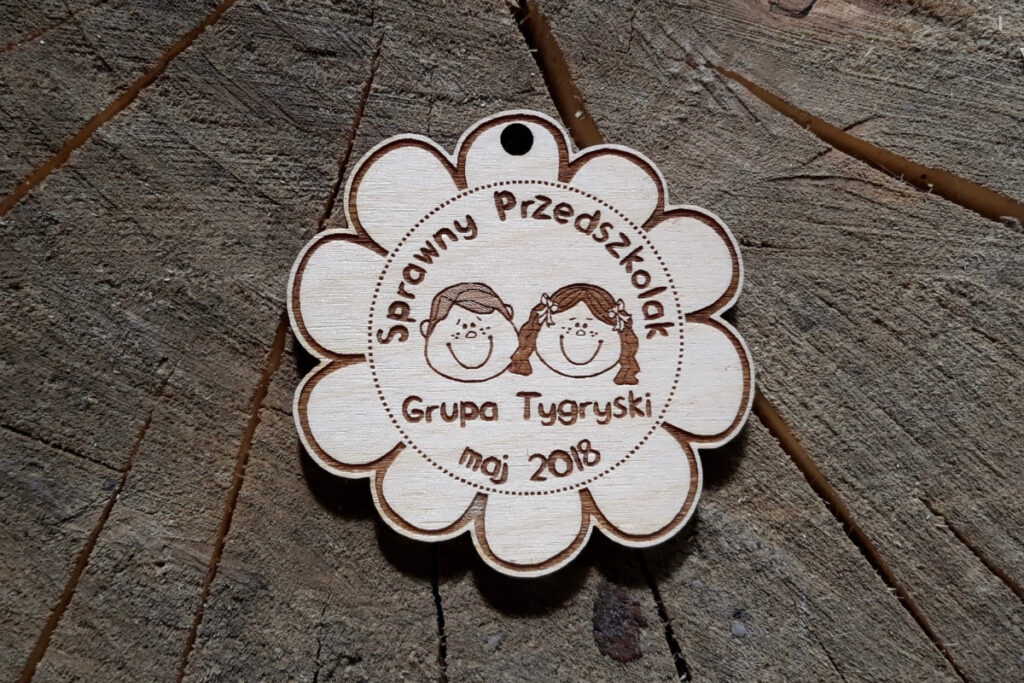 Drewniany medal w kształcie płatka kwiata "Sprawny Przedszkolak" z grawerem uśmiechniętych dzieci  dedykowany grupie "Tygryski" w przedszkolu.