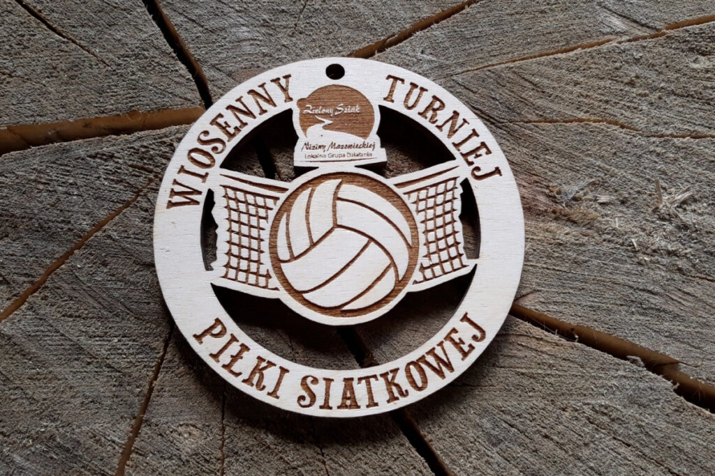 Okrągły, ażurowy medal drewniany na Wiosenny Turniej Piłki Siatkowej z wyciętym motywem siatki, grawerowaną piłką oraz logiem.