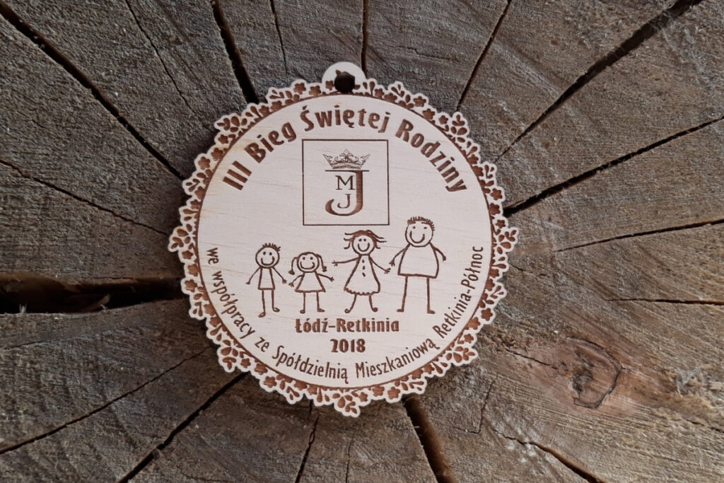 Drewniany medal pamiątkowy na III Bieg Świętej Rodziny z wygrawerowaną 4 osobową rodziną na środku.
