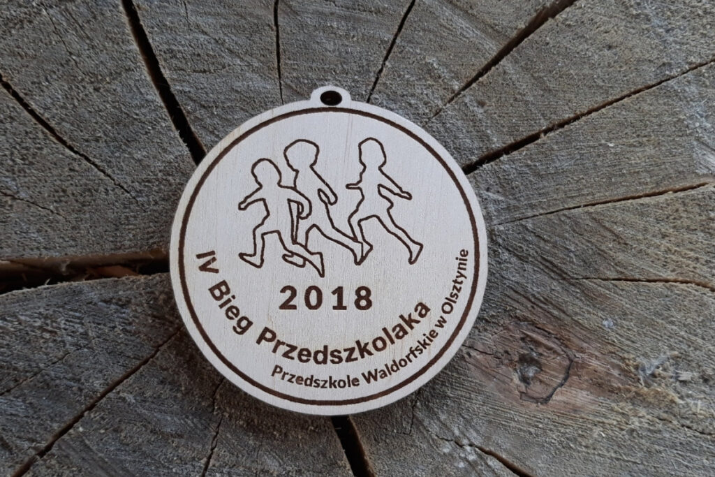 Drewniany medal dla dzieci na IV Bieg Przedszkolaka z grawerem biegnących postaci dzieci.