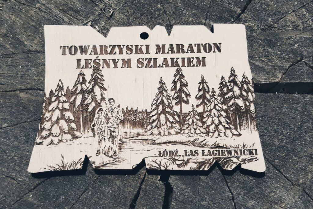 Drewniany medal o nieregularnym kształcie plastra drewna z grawerem maratończyków biegnących przez las.