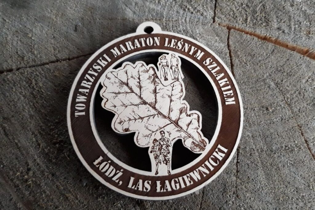 Okrągły drewniany medal o konstrukcji ażurowej z precyzyjnie wyciętym i wygrawerowanym kształtem liścia, zawieszony na ekologicznym sznurku.