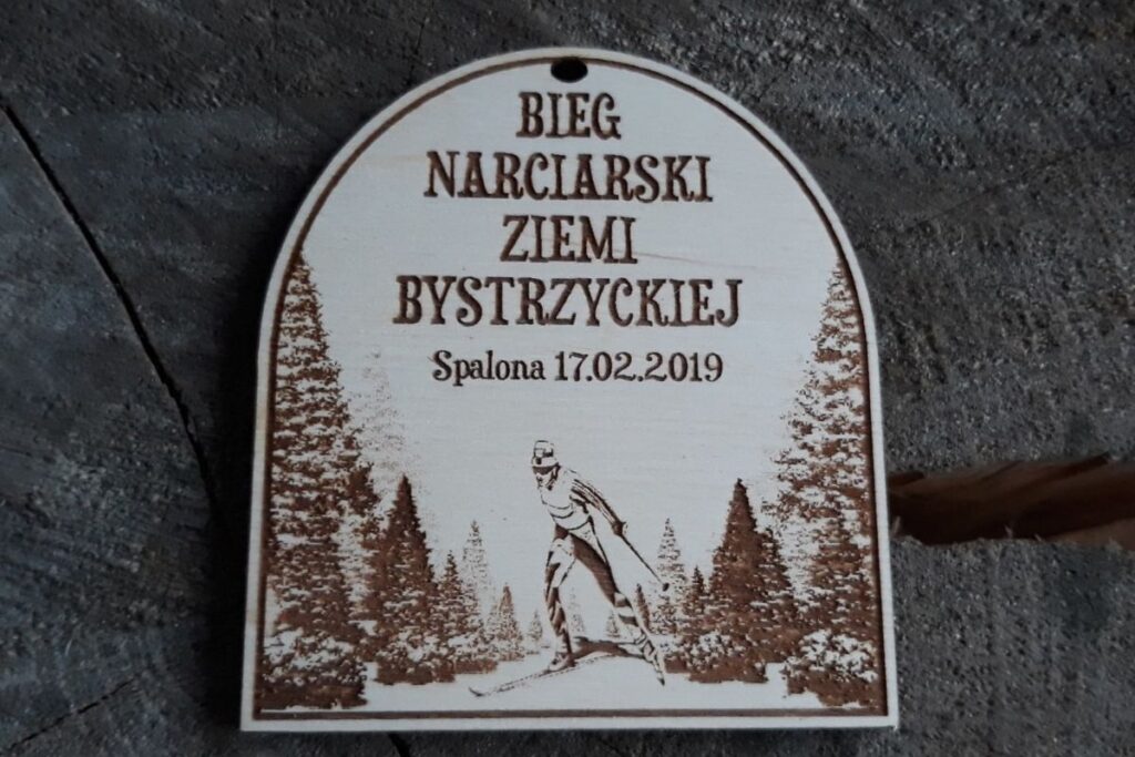 Drewniany medal pamiątkowy z Biegu Narciarskiego Ziemi Bystrzyckiej 2019 w Spalonej z grawerem narciarza.