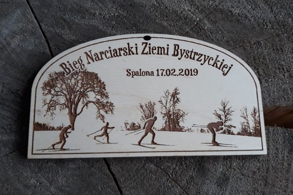 Drewniany medal pamiątkowy z Biegu Narciarskiego Ziemi Bystrzyckiej 2019 w Spalonej z grawerem narciarza.