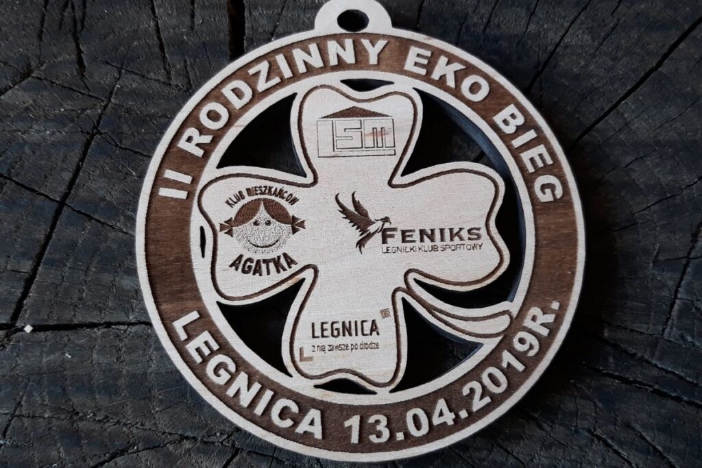 Drewniany medal okrągły z ażurowo wyciętą czterolistną koniczyną w środku i napisem II Rodzinny Eko Bieg Legnica.
