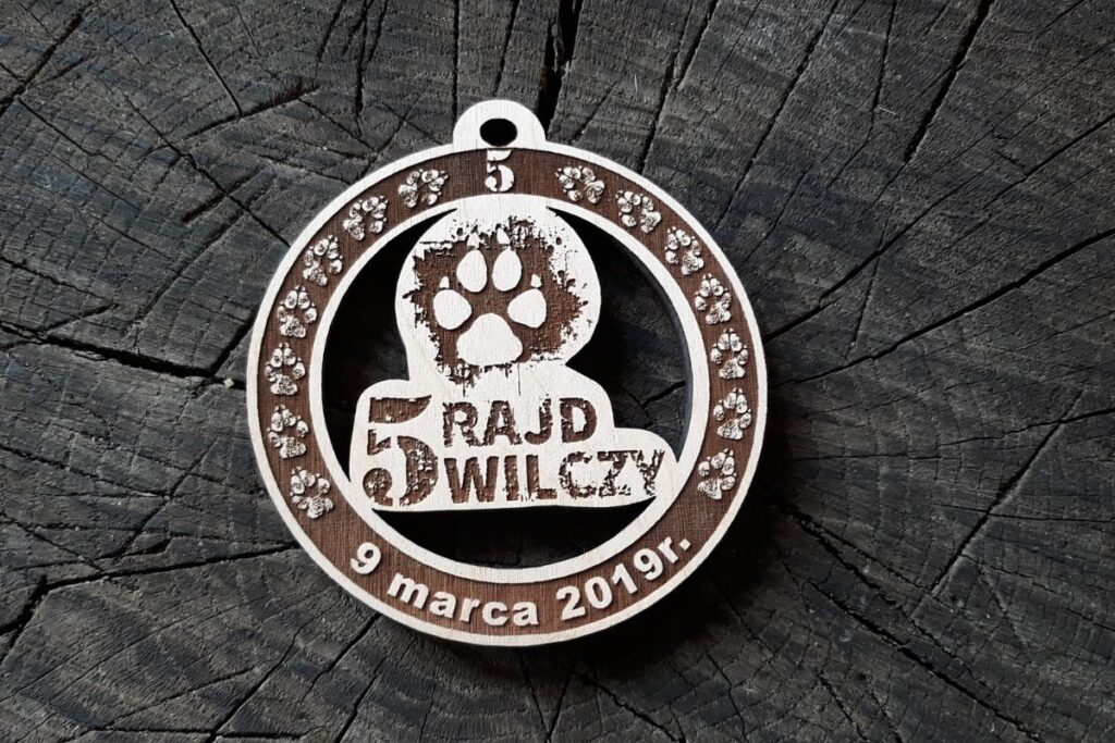 Drewniany medal na 5. Rajd Wilczy z ażurowym wycięciem łapy wilka i grawerowaną tekstem.