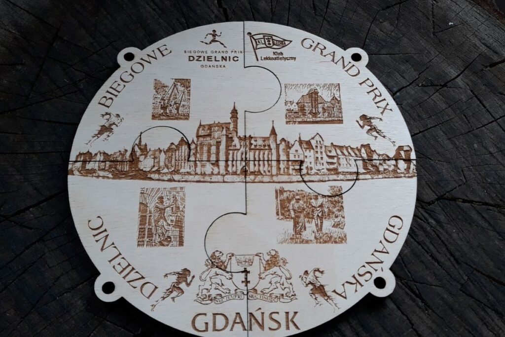 Drewniana tabliczka pamiątkowa Biegowego GP Dzielnic Gdańska złożona z czterech medali tworzących panoramę miasta.