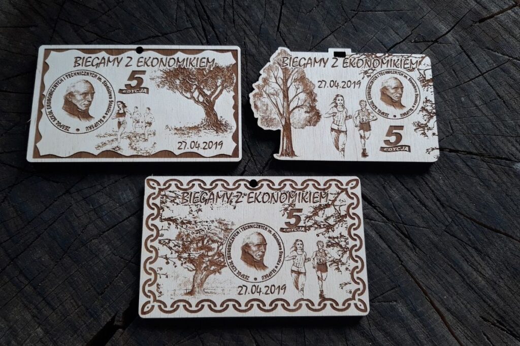 Drewniany medal na 5. Bieg z Ekonomikiem, grawerowany laserowo z logo szkoły i motywem biegacza. Na zdjęciu 3 propozycje medali.
